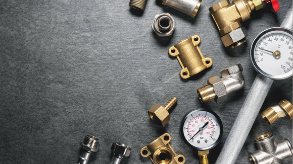 Plumbing tools and parts arranged on a dark, textured surface, including gauges and brass fittings.