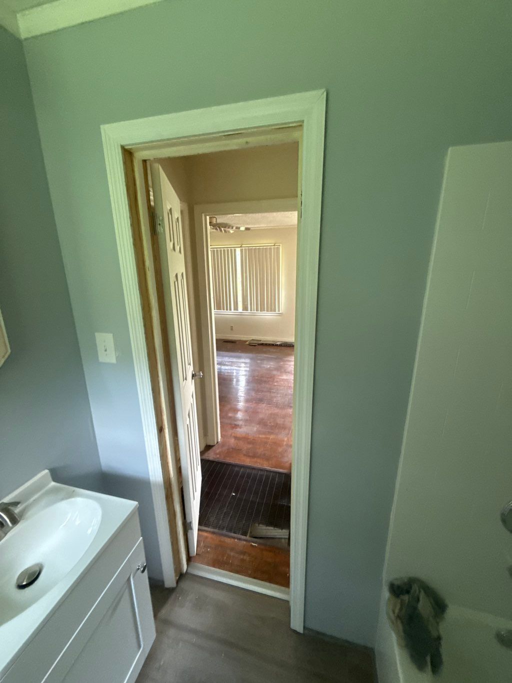 Bathroom doorway leading to a room with hardwood floors, a window with curtains, and gray walls.