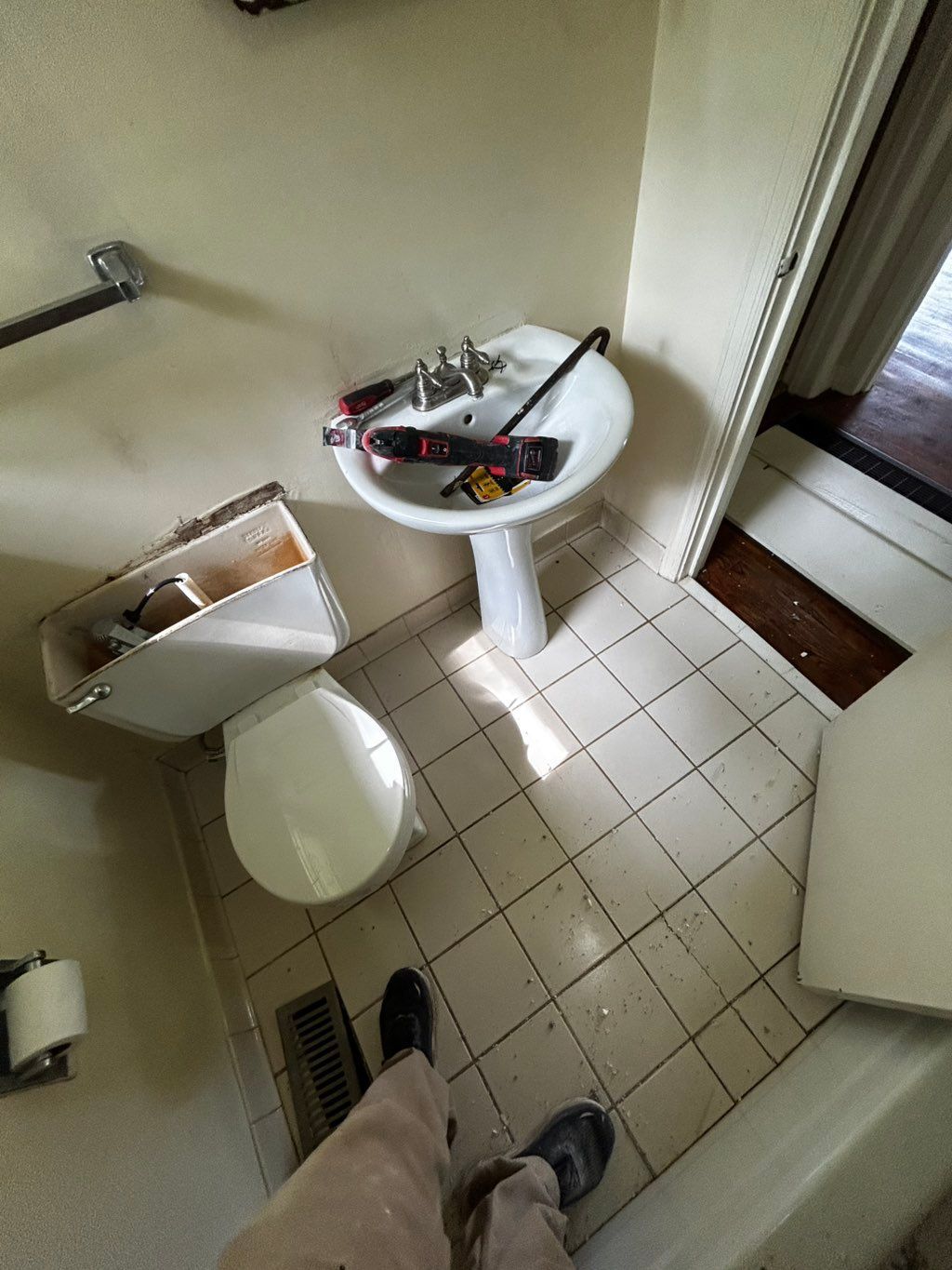 Bathroom renovation in progress: pedestal sink, toilet, tools, and open wall reveal.