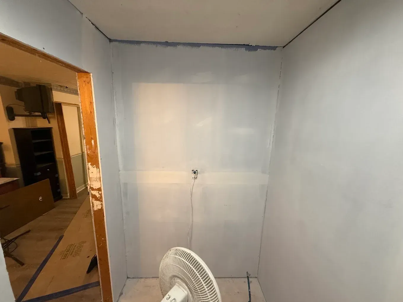 Interior room with painted light blue walls and an open doorway. A fan sits on the floor.
