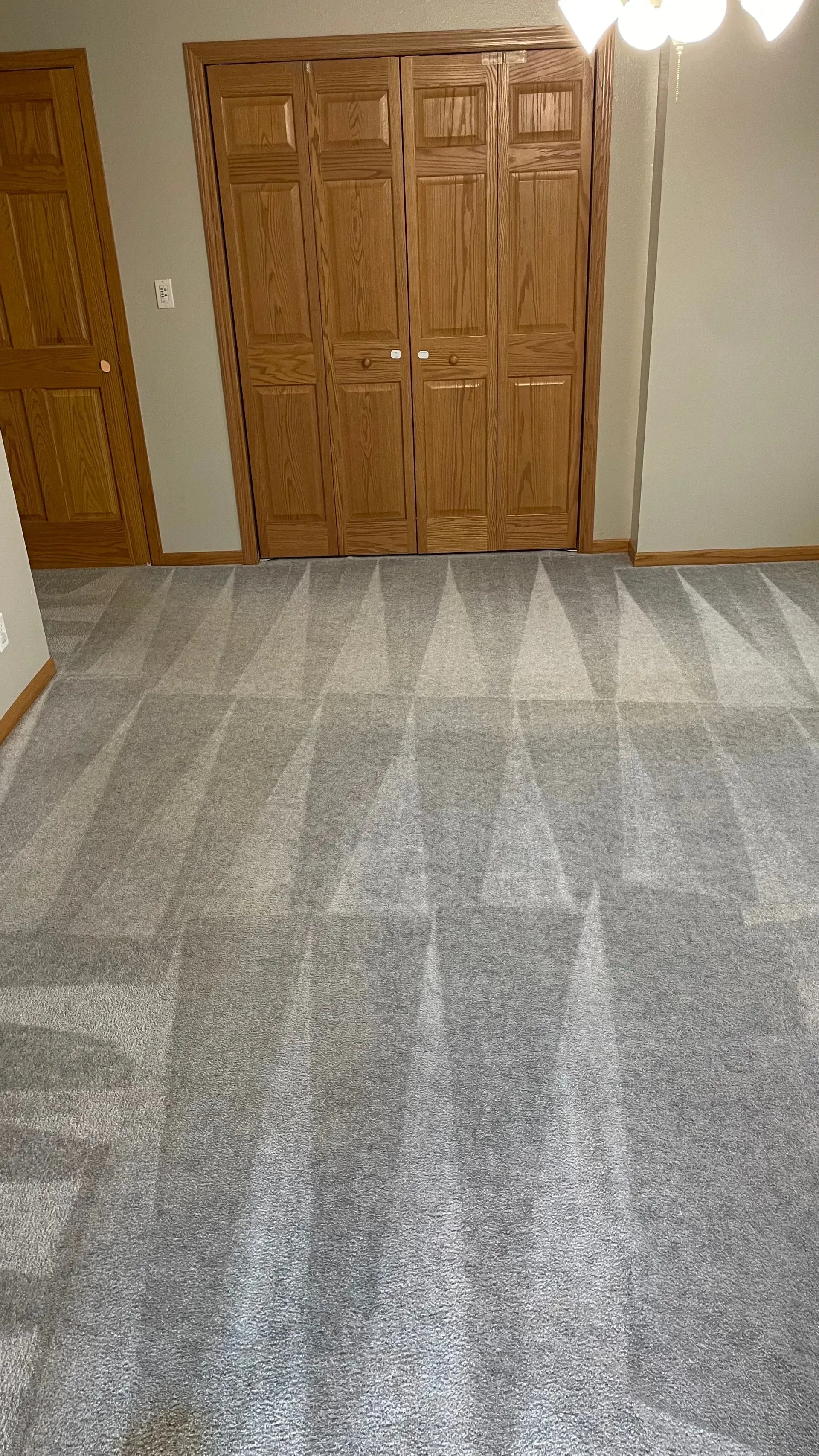 A room with light grey carpet and wood closet doors.