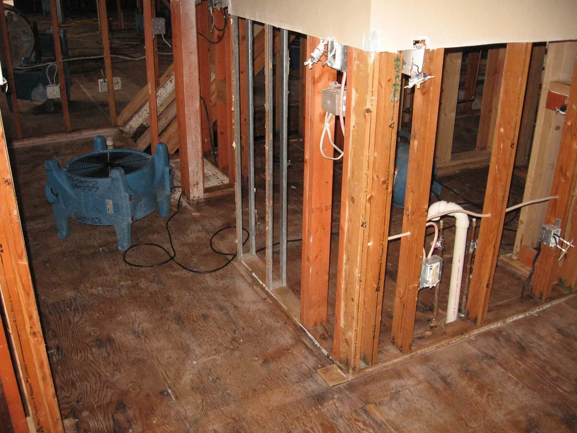 Interior demolition; exposed wall studs, flooring, plumbing, electrical fixtures, blue fan.
