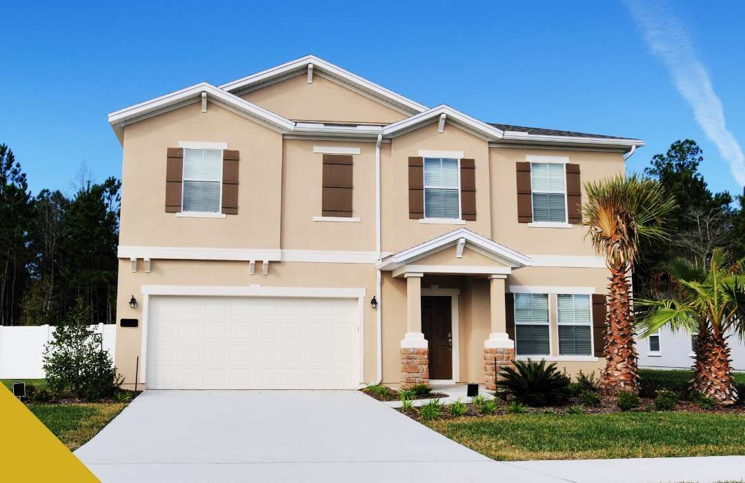 Beige two-story house with a white garage, brown shutters, and palm trees against a blue sky.