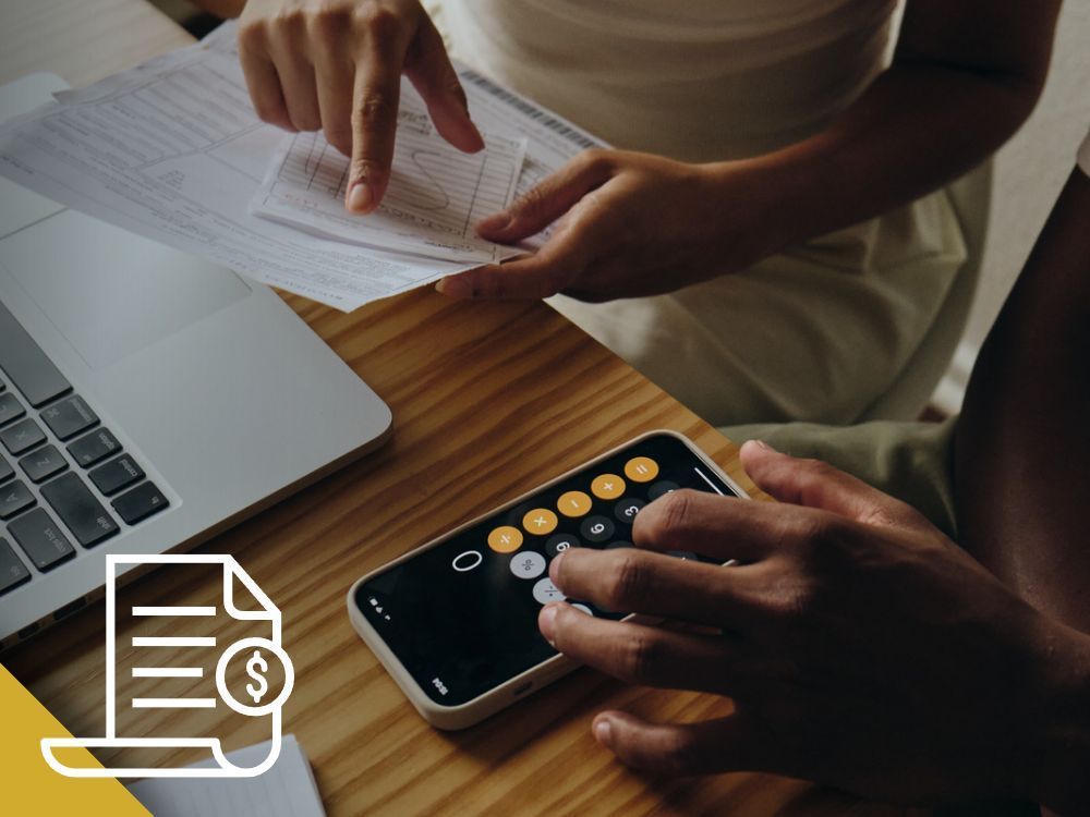 Two people calculating finances with a phone calculator and paperwork on a wooden desk.