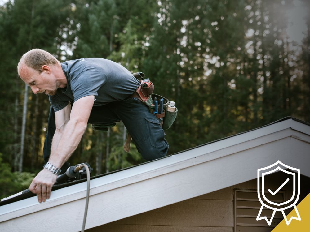 Roofer on a roof, installing a gutter, wearing a tool belt.