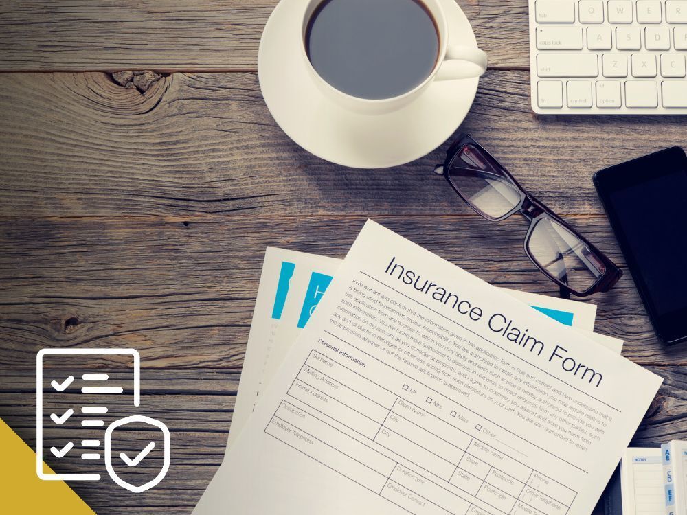 Insurance claim form on wooden desk with coffee, glasses, phone, and keyboard.