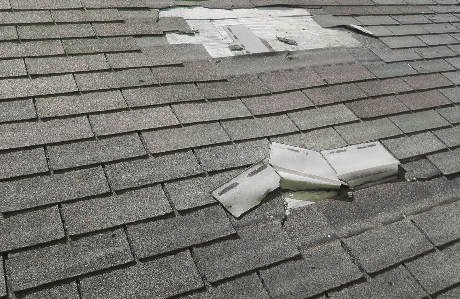 Damaged gray asphalt shingle roof with missing shingles and exposed underlayment.
