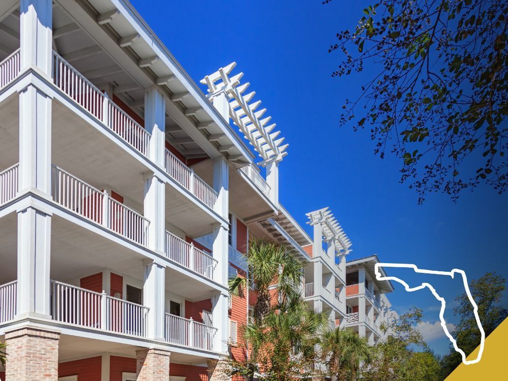 Multi-story red and white building with balconies under a blue sky, Florida outline overlay.