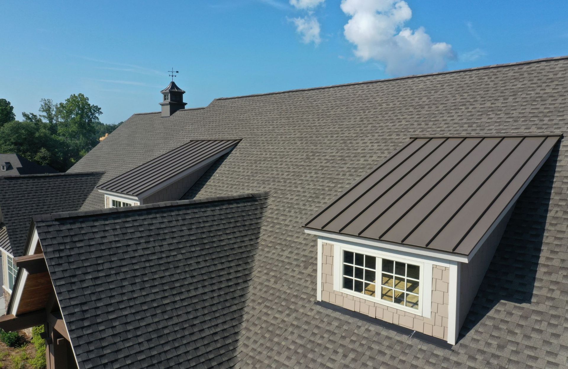 A brown shingled roof with metal dormer windows under a bright blue sky.