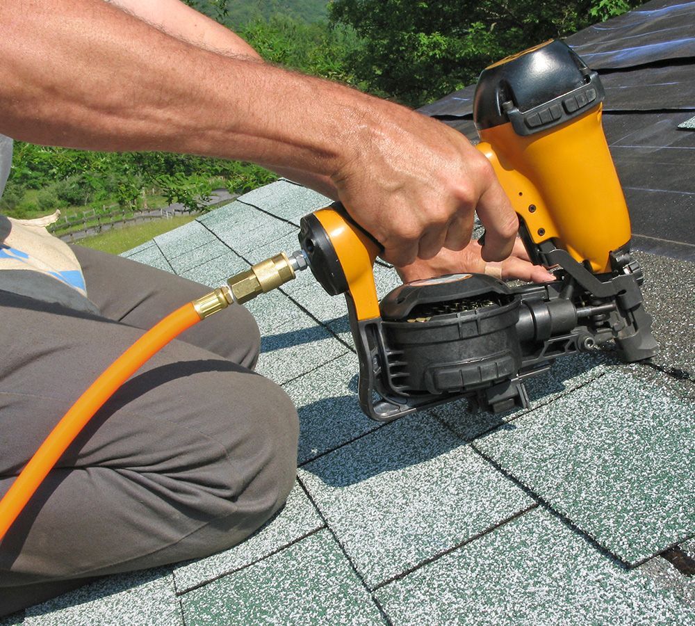 Person using a pneumatic nail gun on a shingled roof. Yellow gun, orange hose.
