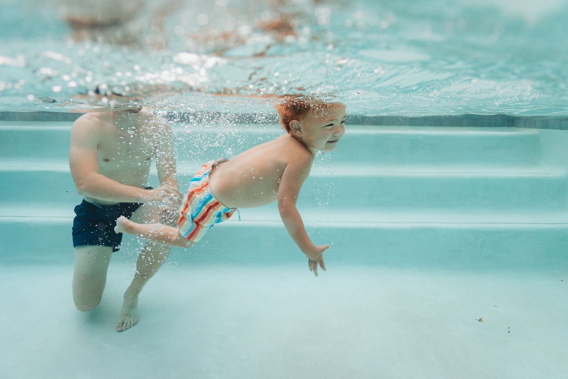 A man and a child are swimming underwater in a swimming pool.