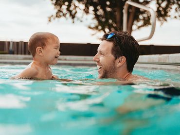 A man and a baby are playing in a swimming pool.