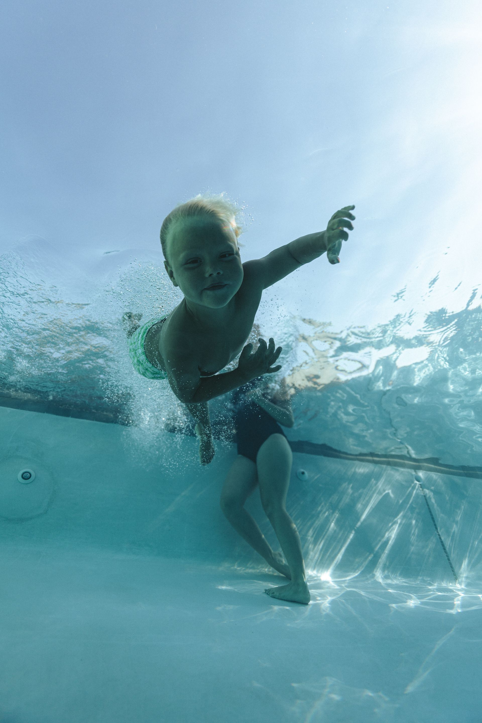 A baby is swimming underwater in a swimming pool.