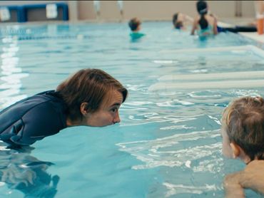 A woman is teaching a child how to swim in a swimming pool.