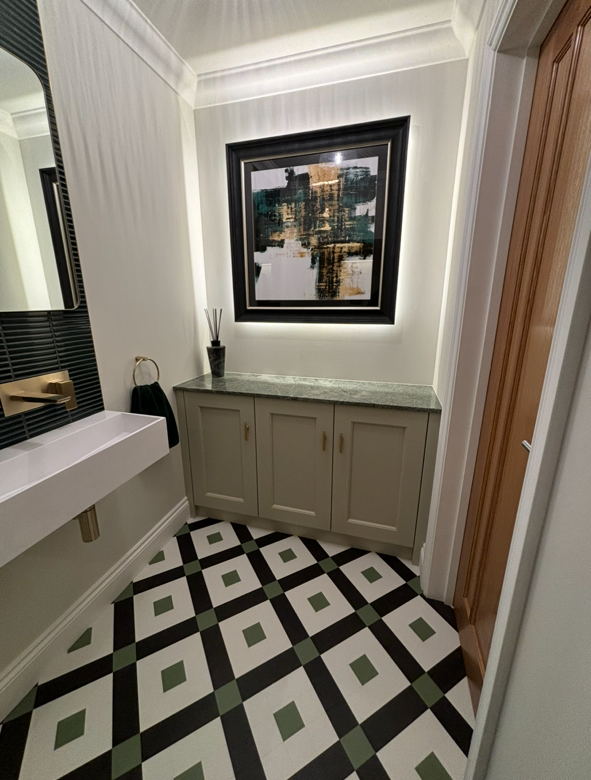 A modern bathroom featuring a white vanity, a green-and-white geometric tiled floor, and an illuminated framed wall art.