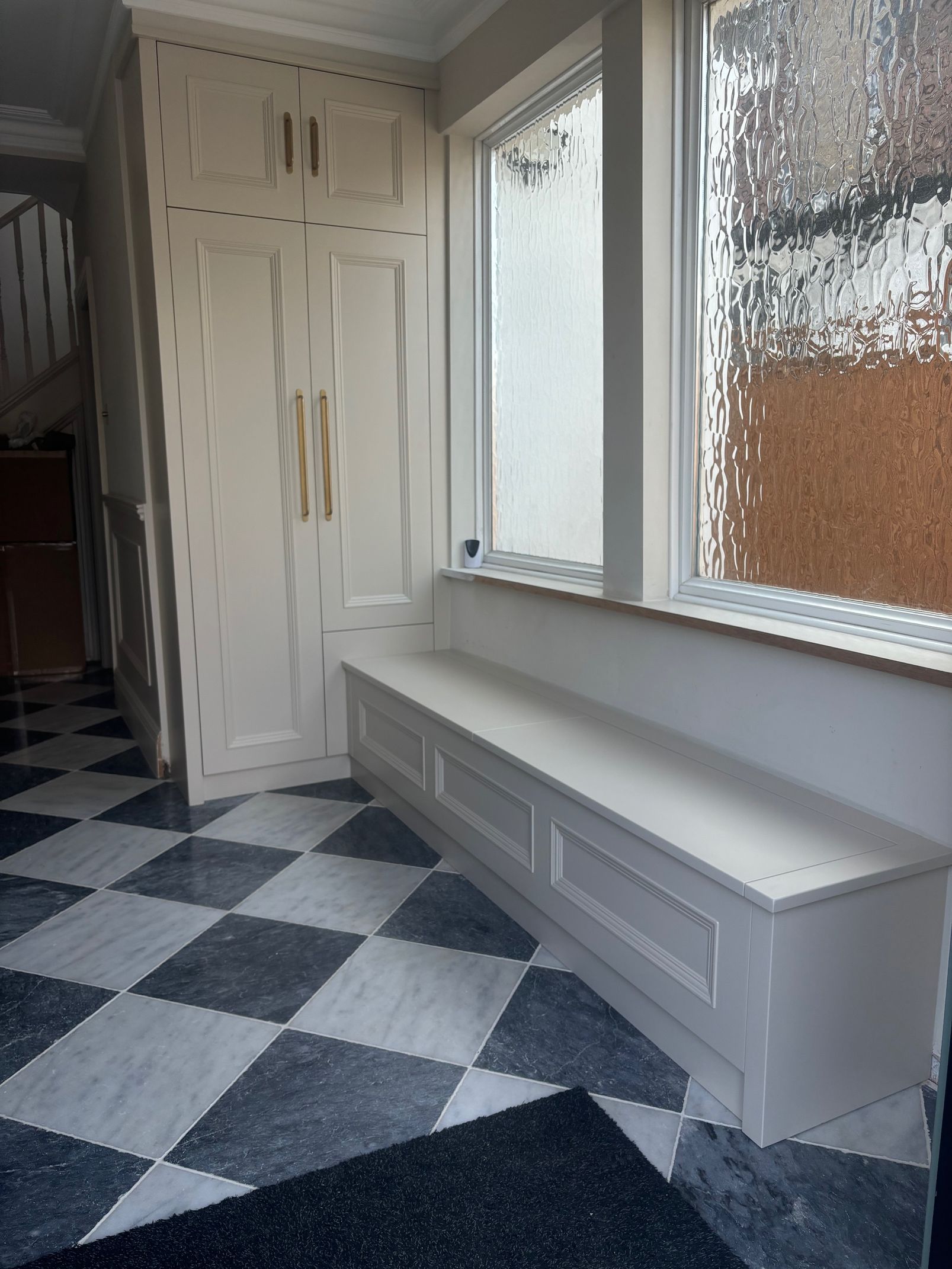 A hallway with a checkerboard floor, built-in cream storage cabinets, and a low window bench seat.