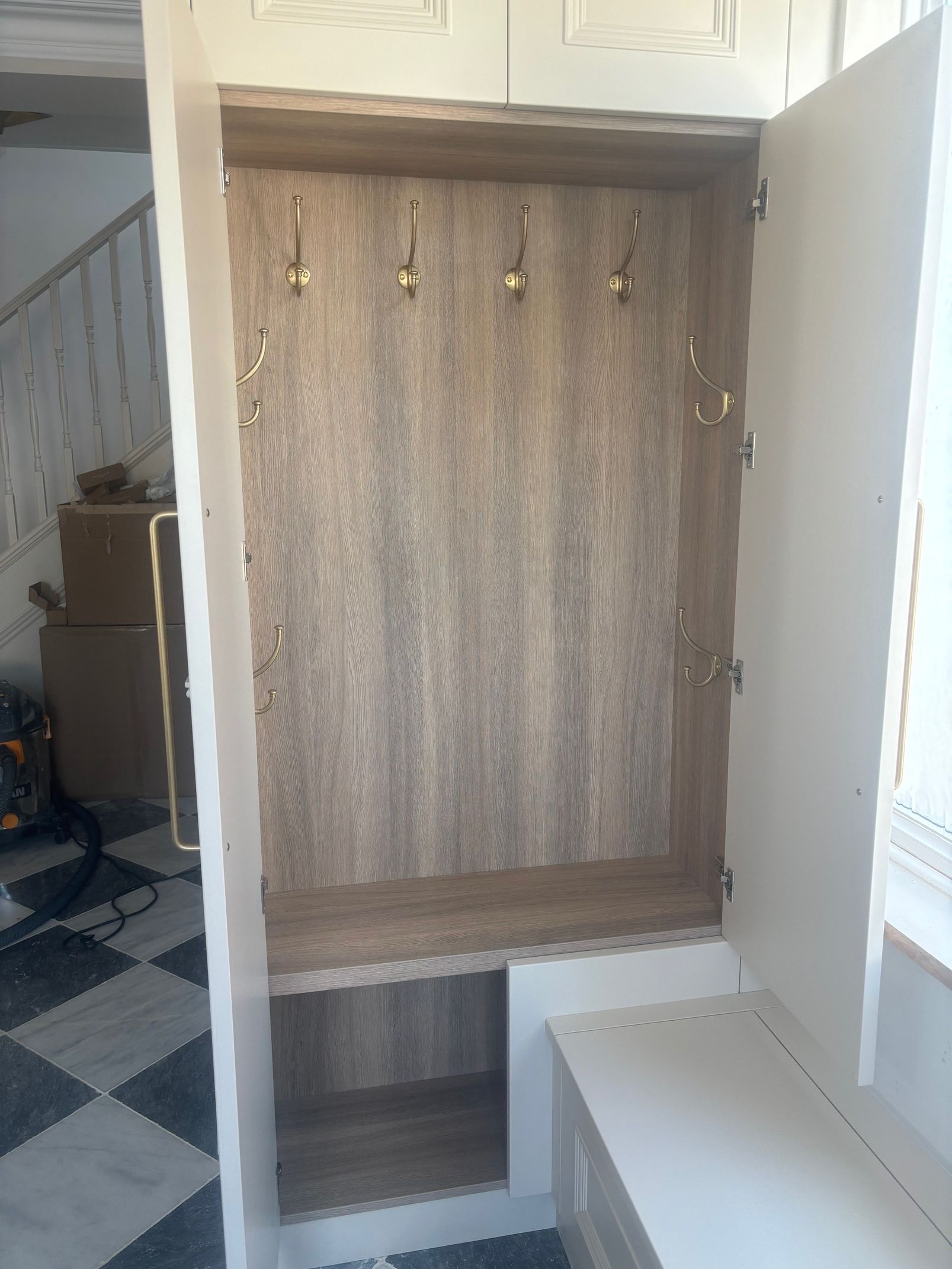 A white entryway coat rack with a wood-grain back panel, four hooks, a lower shelf, and an attached bench seat.