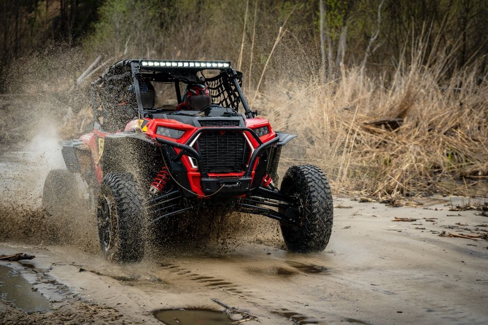 Red Off-road Buggy Splashing Through Mud on a Dirt Trail in a Wooded Area — Cooper's Auto Service Centre in Glen Innes, NSW