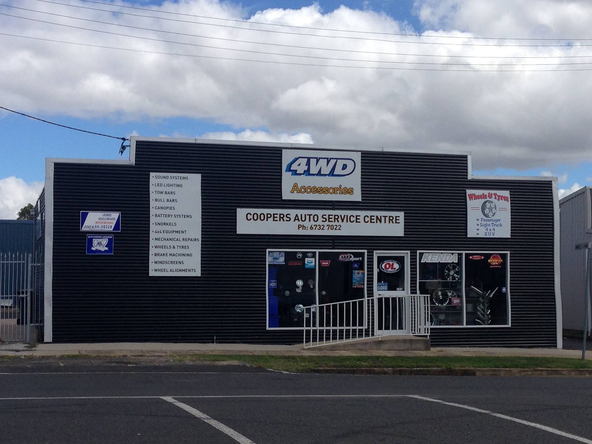 Front view of a 4WD shop with black siding, blue trim, and a cloudy sky overhead