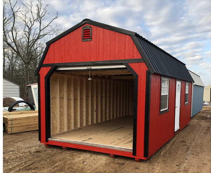 A red barn with a black roof is sitting in the dirt.