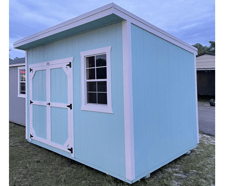 A blue and white shed with a window is sitting in the grass.