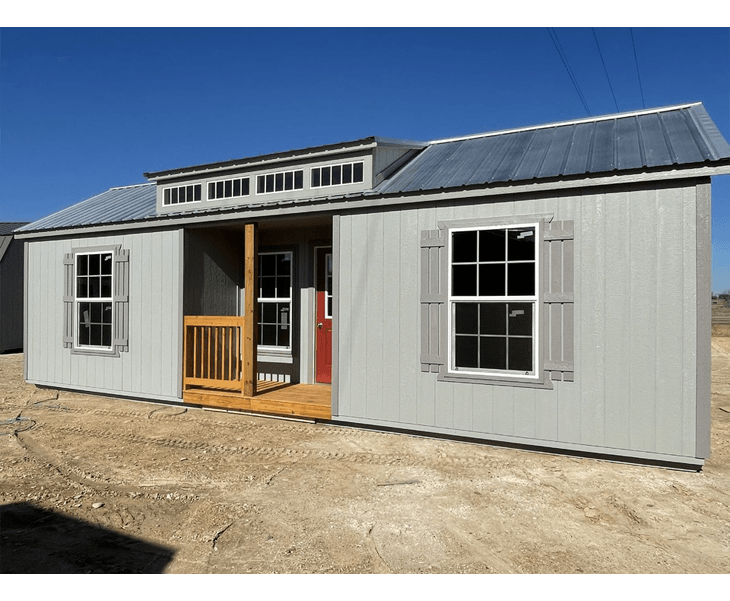 A gray cabin with a porch and two windows