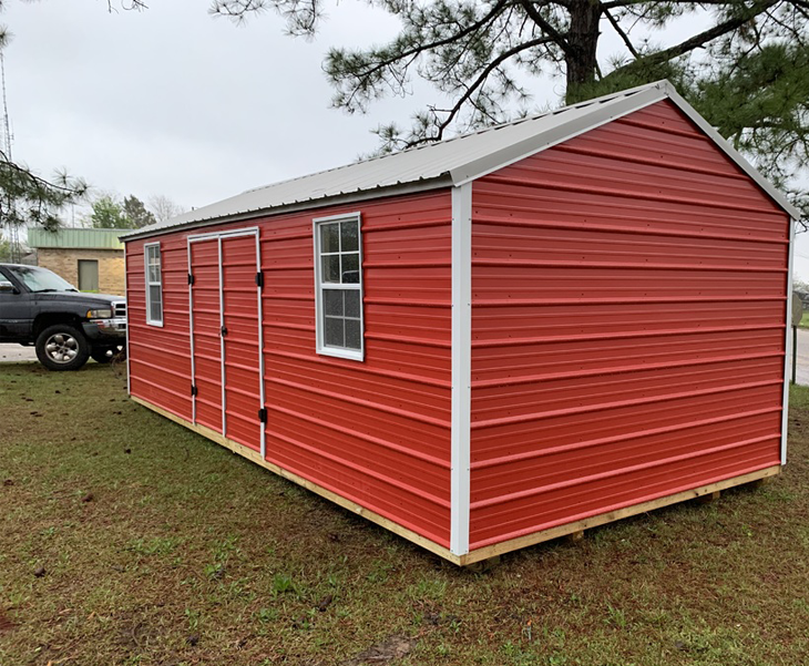 A red shed with a white trim is sitting in a grassy field next to a truck.