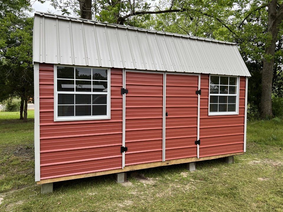 A red shed with a white roof is in the middle of a grassy field.