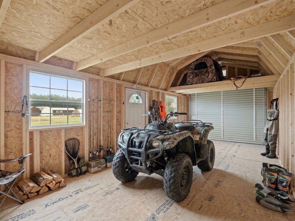 ATV parked inside an unfinished wooden garage with exposed rafters and a window on the left.