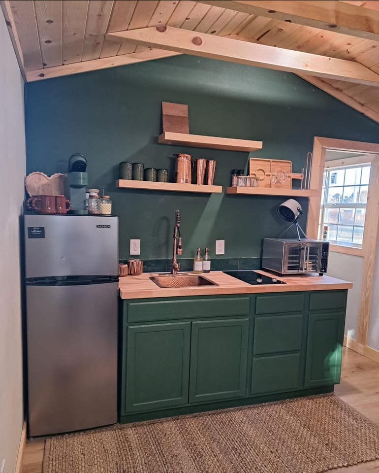A kitchen with green cabinets , a refrigerator , a sink , and a microwave in a Portable Building