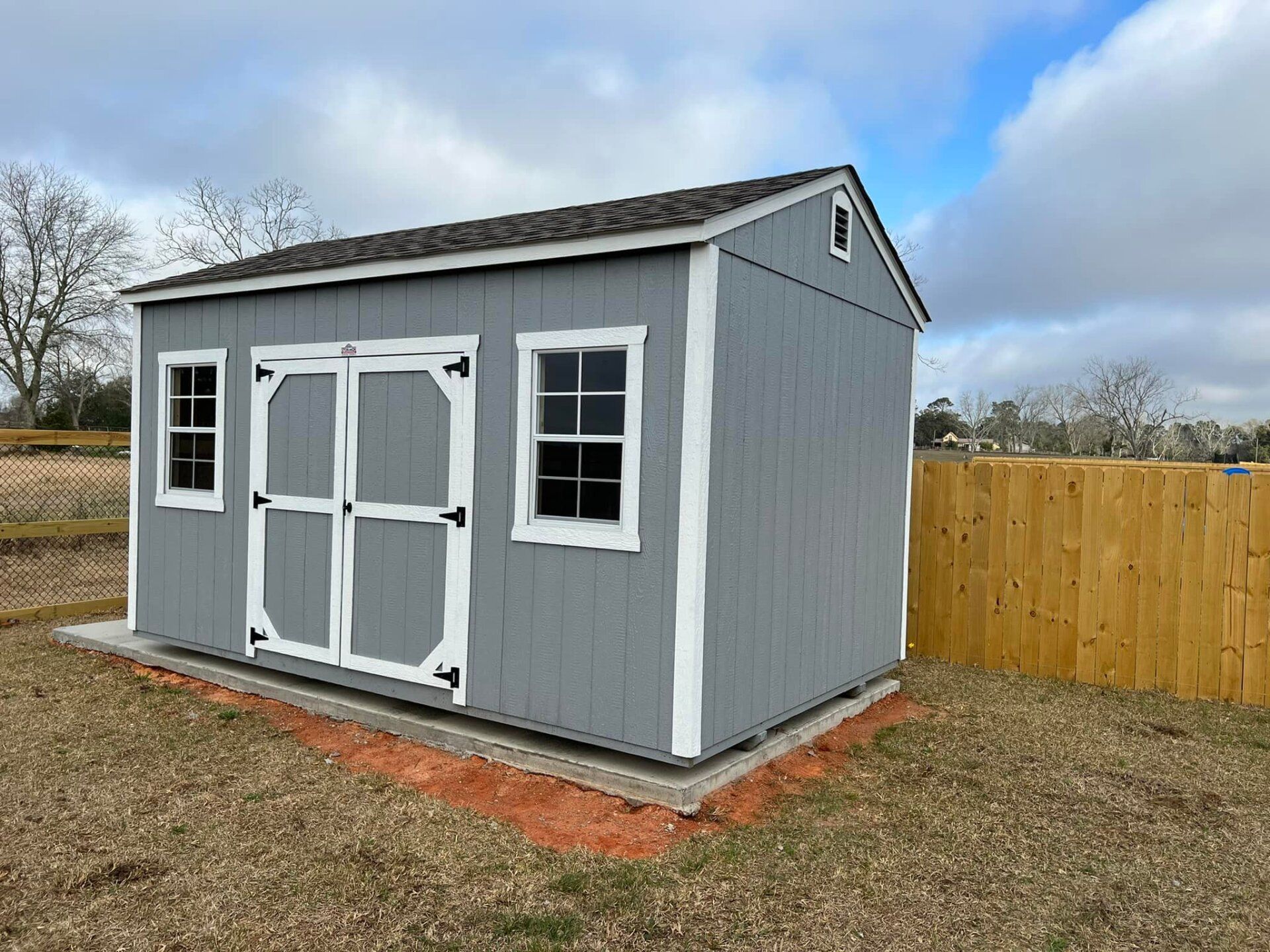 A gray and white shed with a wooden fence in the background.