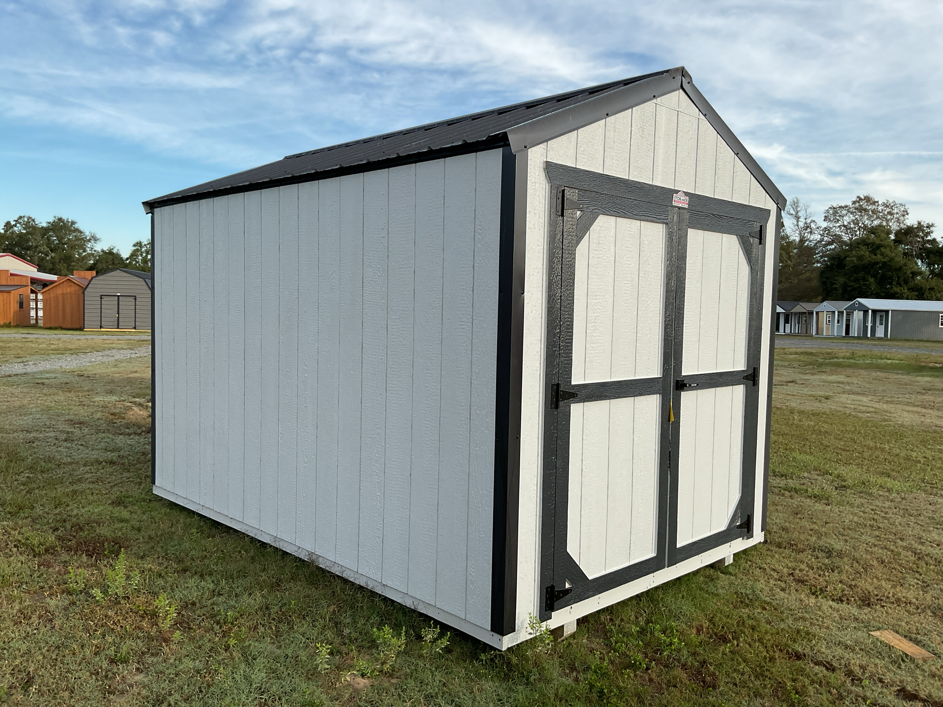 Small white outdoor shed with black trim on a grassy lot under a blue sky