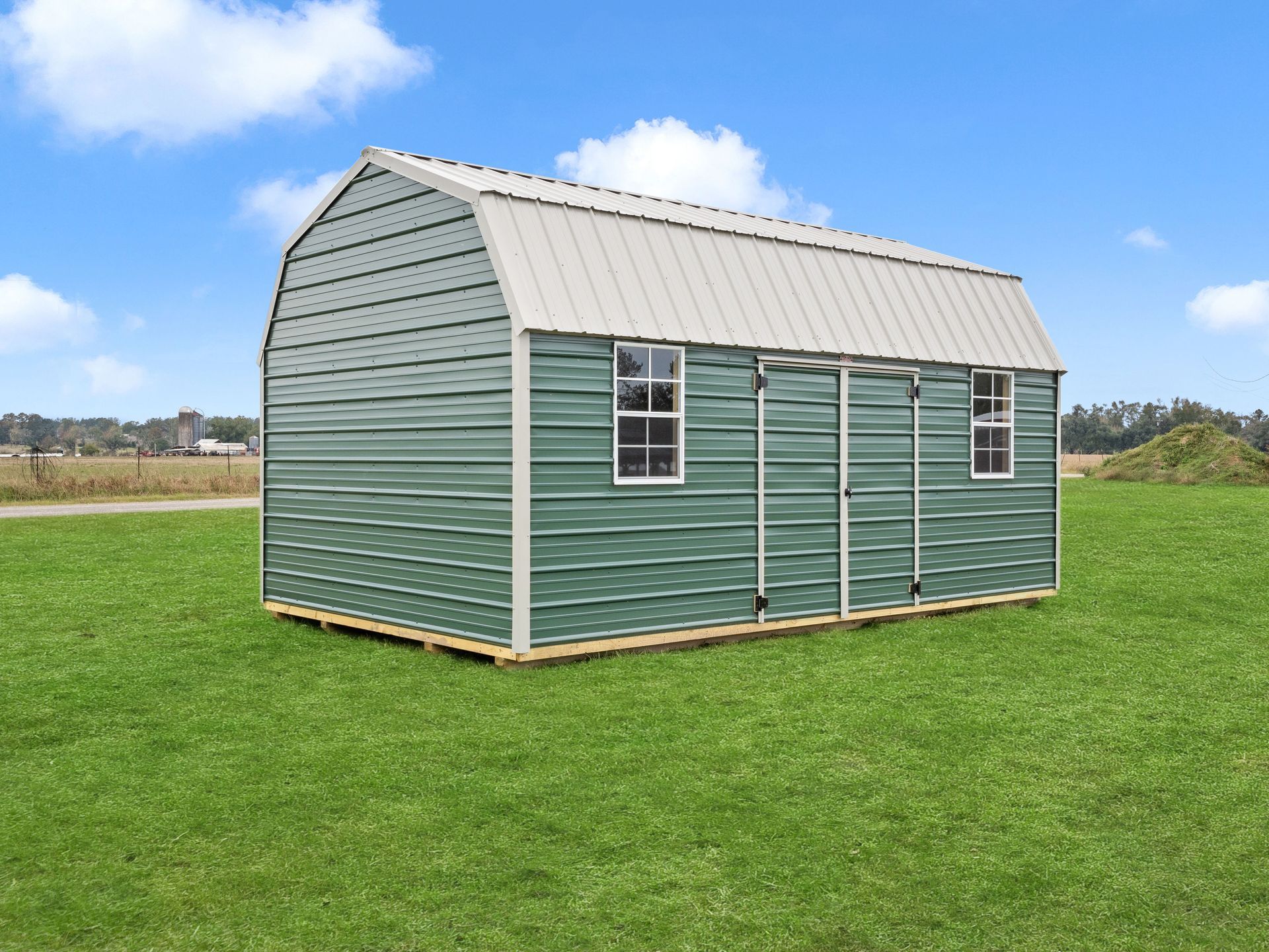 A green barn is sitting on top of a lush green field.