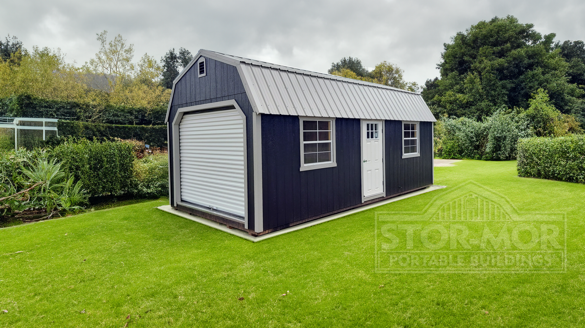 A navy blue barn with a garage door is sitting in the middle of a lush green field.