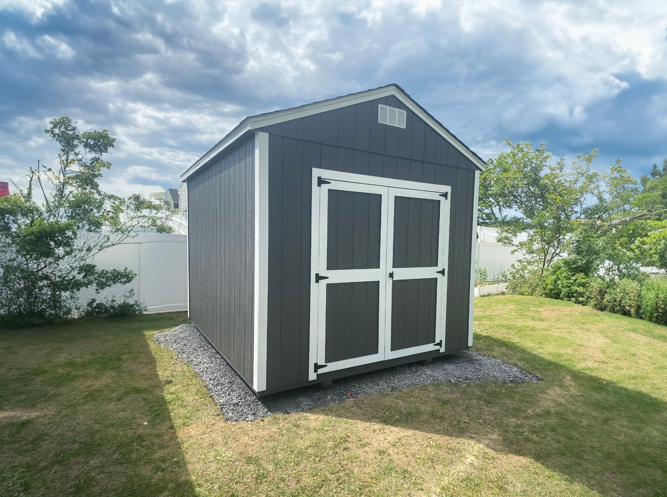 A gray and white shed is sitting in the middle of a grassy field.