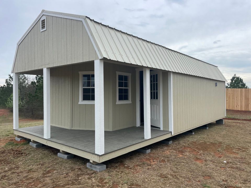 A deluxe barn cabin with a porch and a metal roof is sitting in the middle of a field.