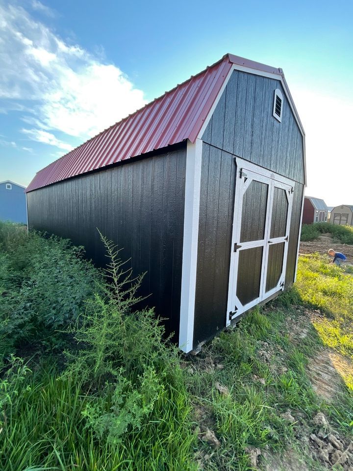A black barn with a red roof is sitting in the middle of a grassy field.