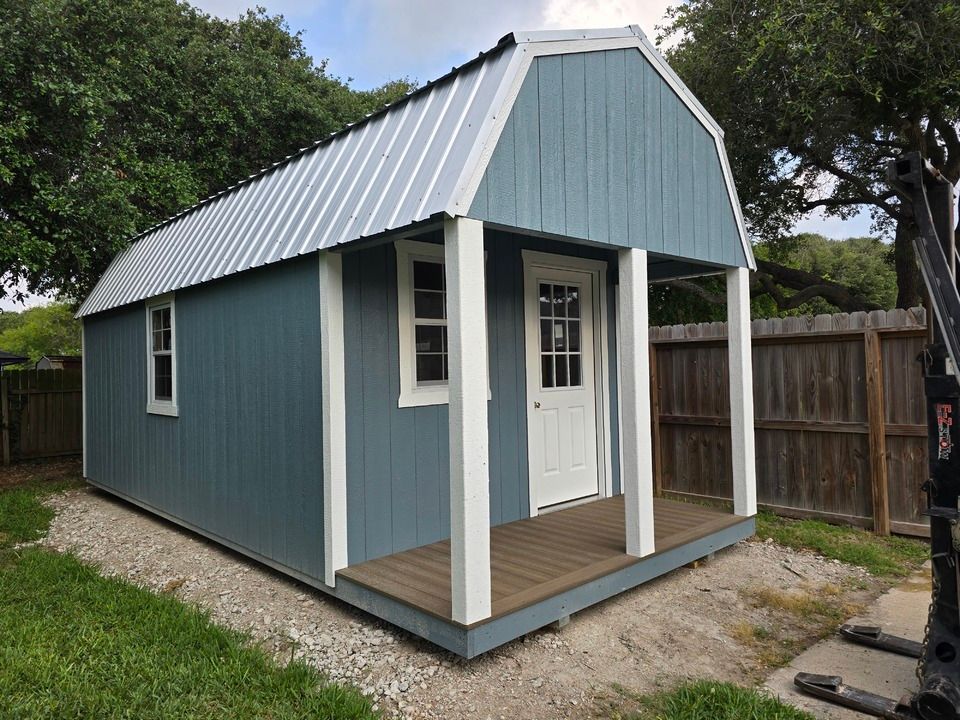 A blue and white barn with a porch and a fence in the background.