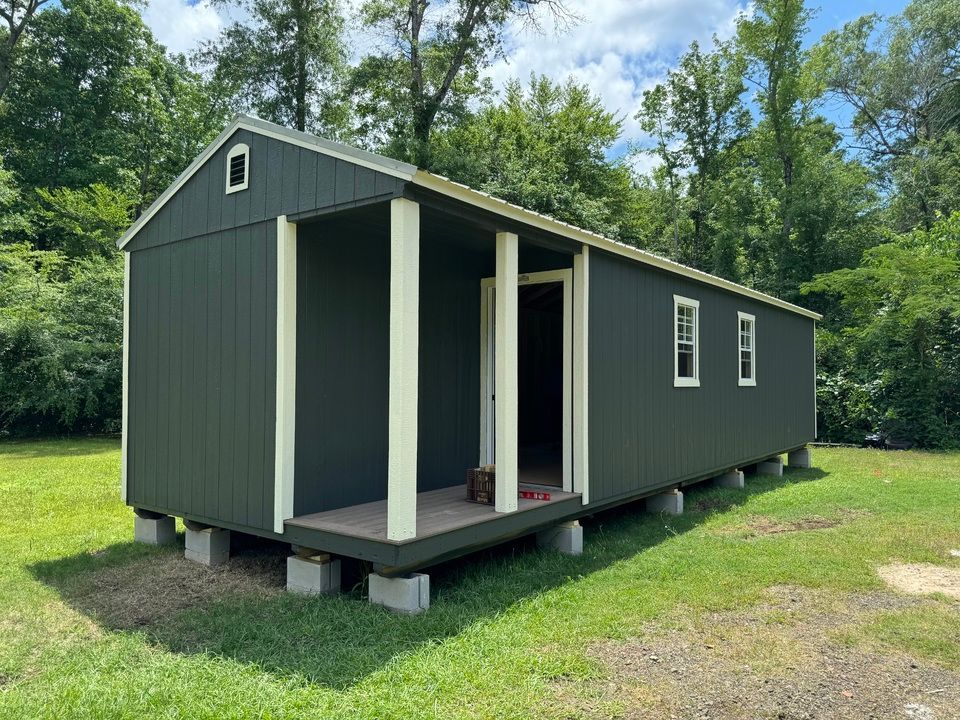A shed with a porch is sitting in the middle of a grassy field.