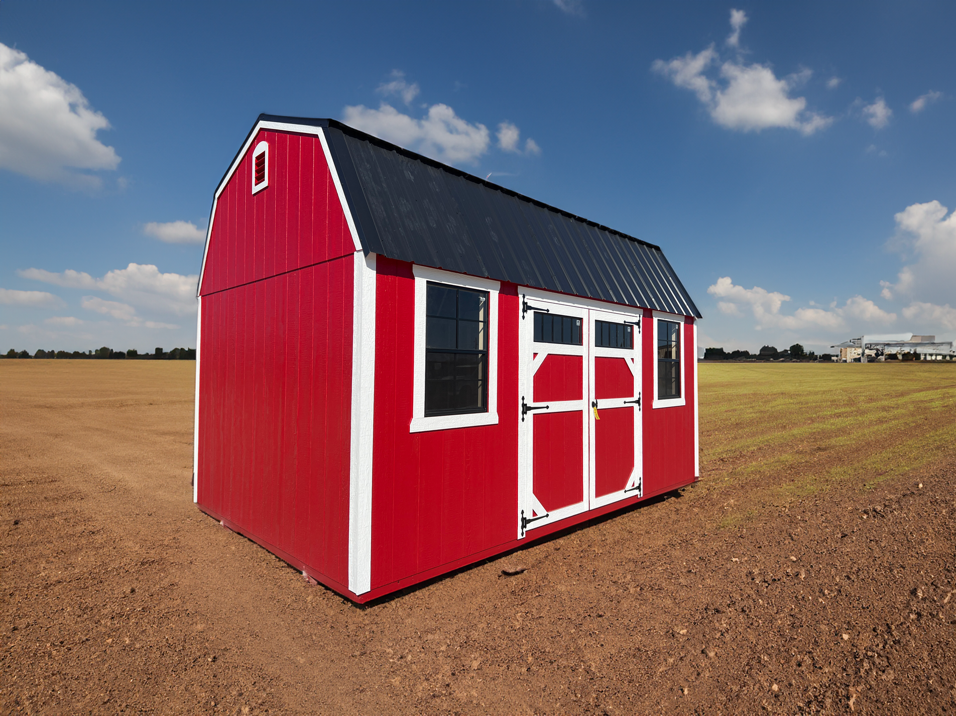A red barn with white trim sits in the middle of a dirt field