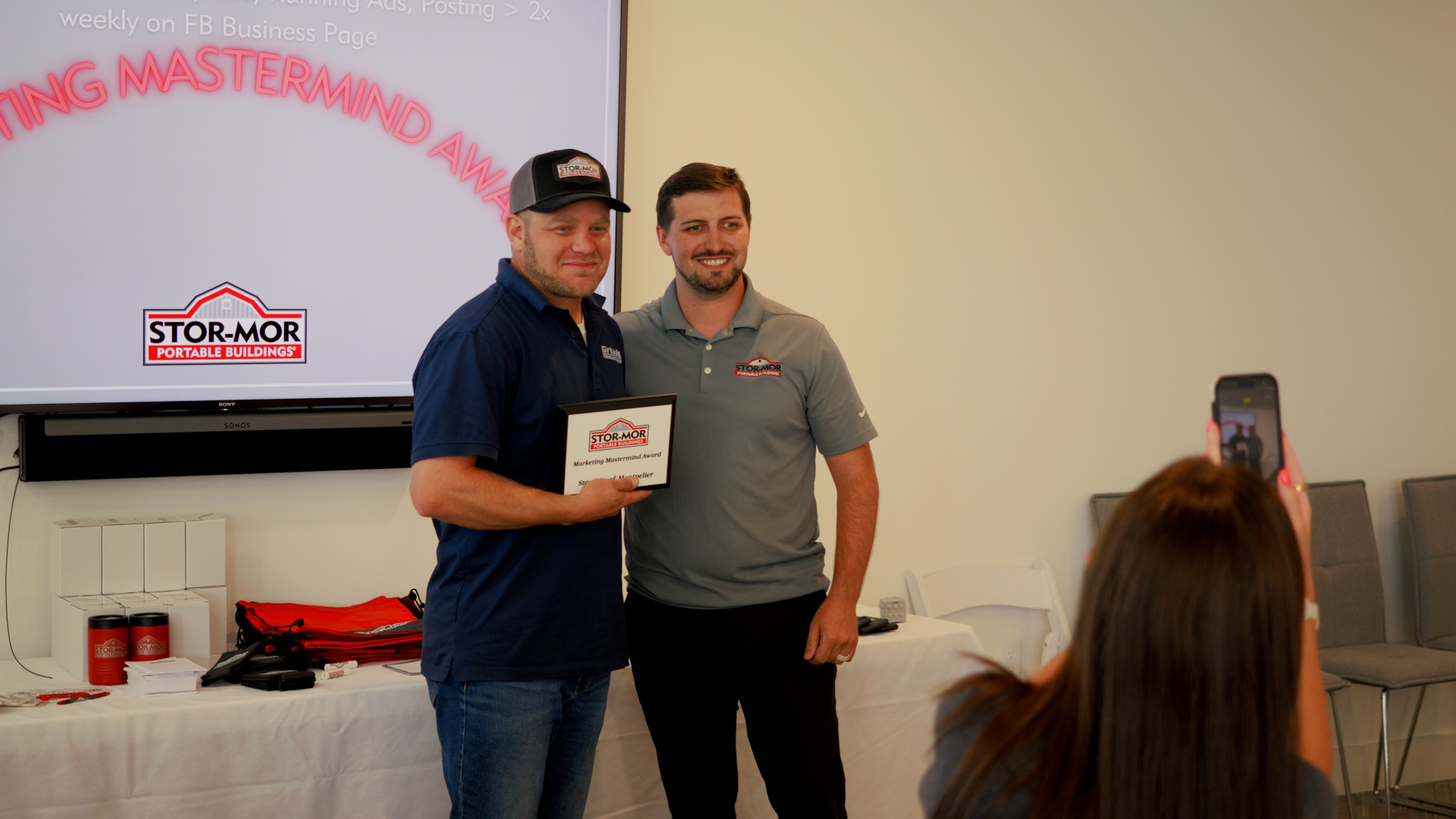 Two men pose with a certificate at a workshop presentation, with a projected slide behind them.