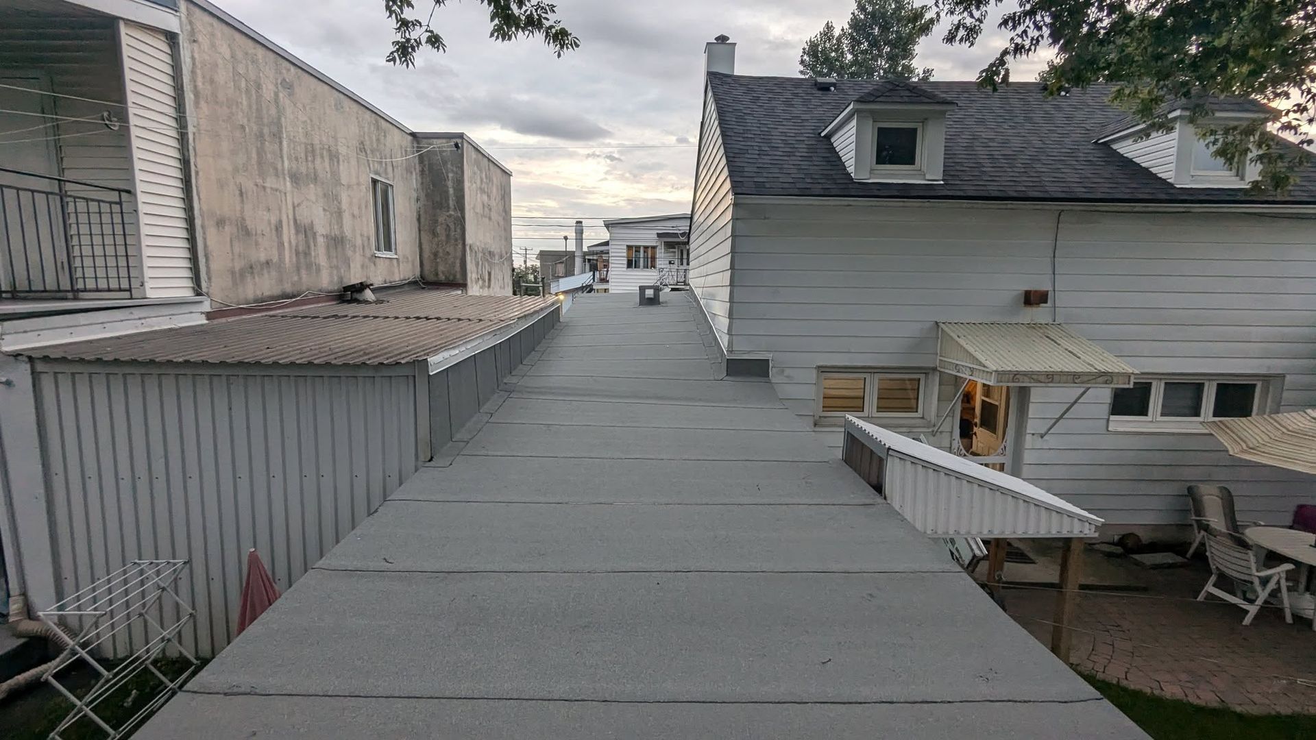 Passerelle étroite sur le toit entre les bâtiments, avec un revêtement gris et un ciel nuageux au-dessus.