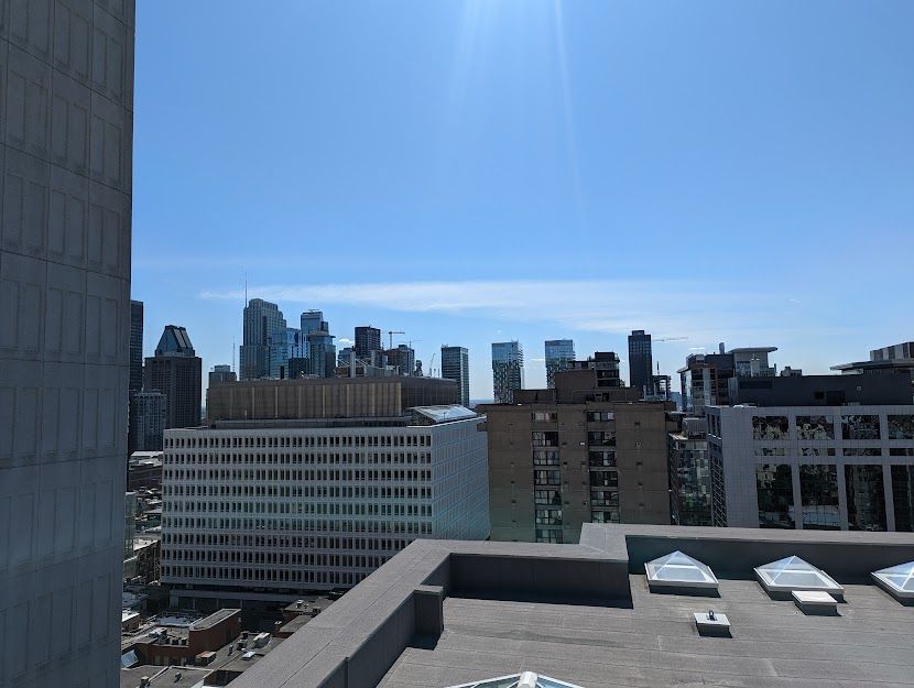 Vue sur la ville depuis un toit, sous un ciel bleu et une lumière du soleil éclatante.