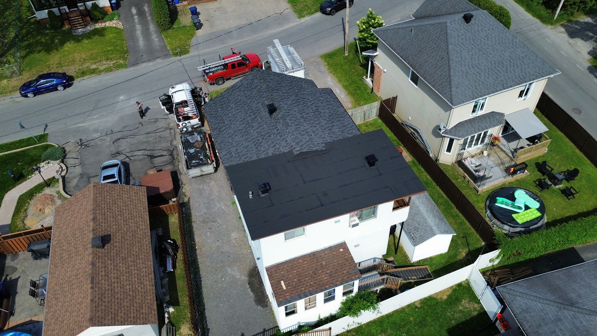 Vue aérienne de maisons de banlieue avec des voitures garées et un camion rouge dans une rue résidentielle.