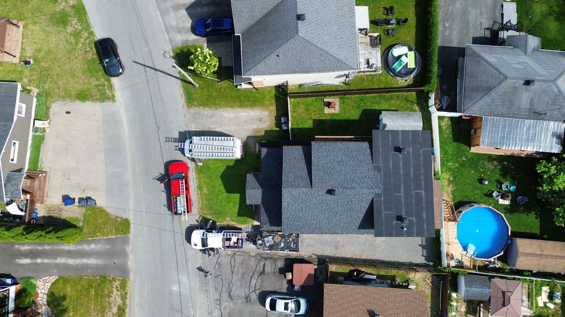 Vue aérienne de maisons de banlieue, de voitures garées et d'une piscine hors sol bleu vif à côté d'une cour clôturée