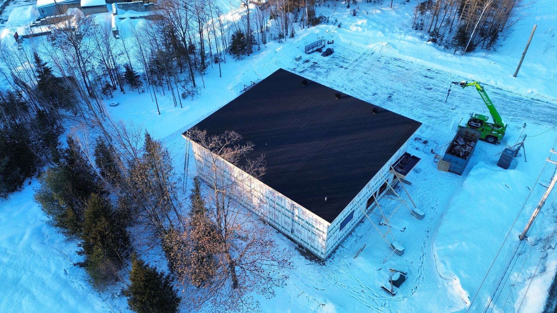 Vue aérienne enneigée d'un bâtiment en construction à côté d'une excavatrice verte et d'équipements épars