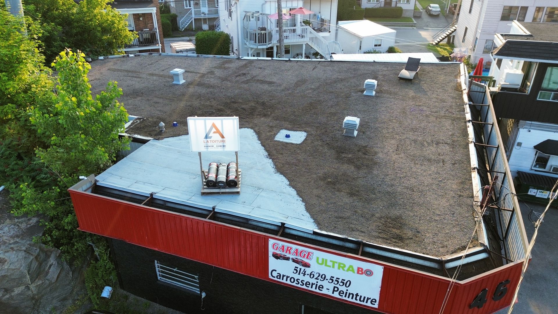 Vue aérienne d'un bâtiment au toit rouge recouvert de gravier et abritant des équipements sur le toit, à proximité d'une rue.