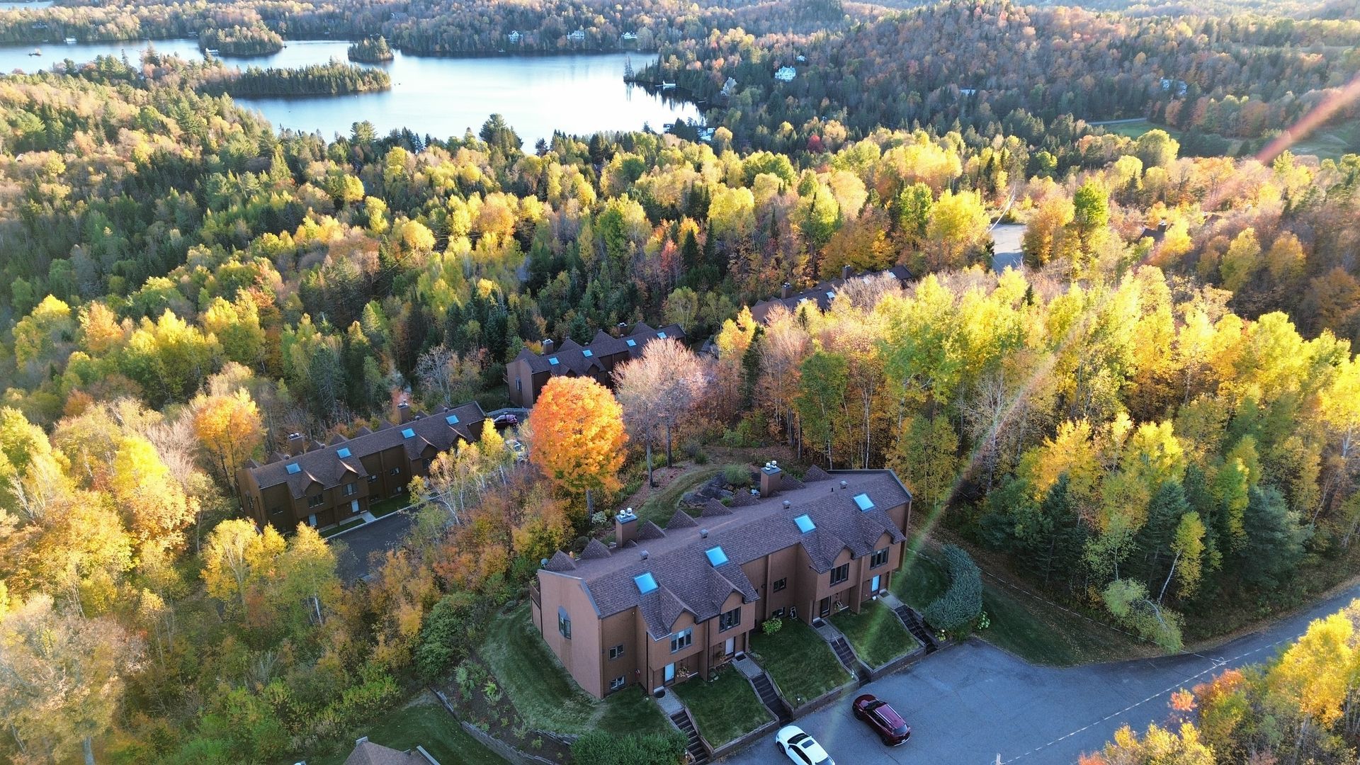Vue aérienne d'un bâtiment en briques en bord de route, entouré d'arbres aux couleurs automnales près d'un lac.