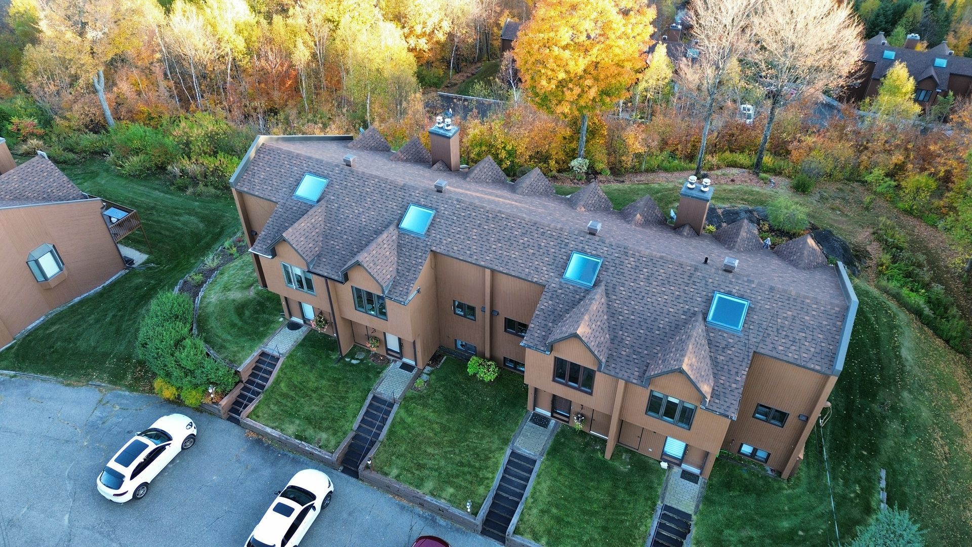 Vue aérienne de maisons de ville brunes avec des puits de lumière bleus, des marches d'entrée, des voitures garées et des arbres d'automne à proximité