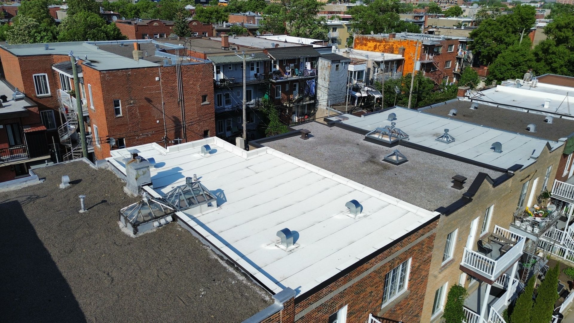 Vue aérienne de toits plats dans un quartier résidentiel, dont un toit blanc équipé d'un système de climatisation.